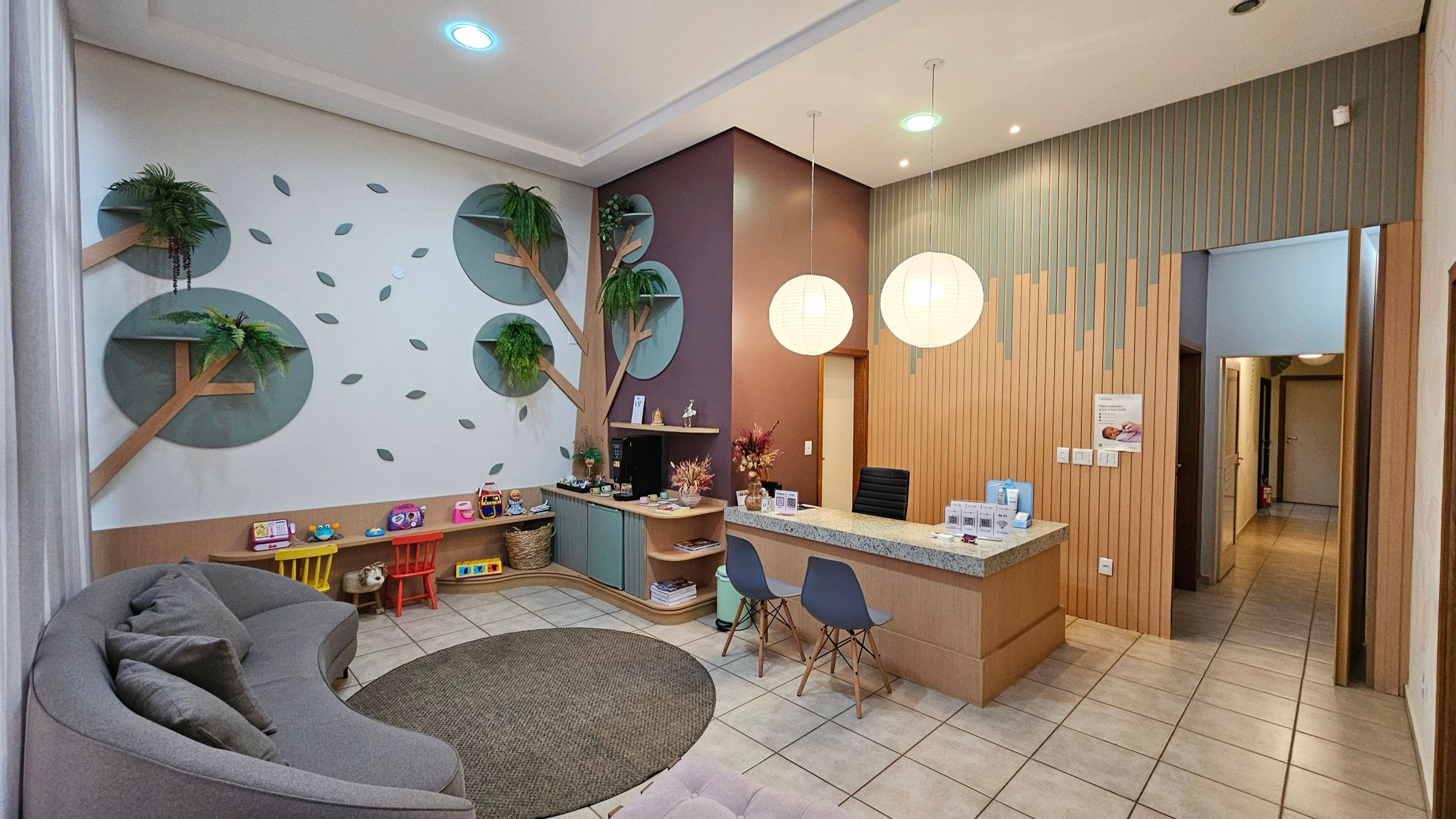 Recepção do Espaço Colo, com sofá, cantinho de brinquedos e balcão de madeira